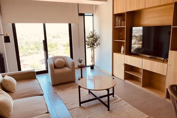 Comedor moderno con mesa redonda, sillas grises tapizadas, escalera de vidrio y aparador de madera con una planta en maceta.
