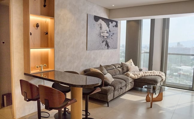 Recámara moderna con cama, sillón y ventanas de piso a techo con vistas a edificios urbanos de ladrillo