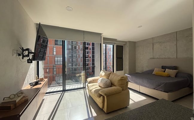 Modern bedroom with bed, armchair, and floor-to-ceiling windows overlooking urban brick buildings